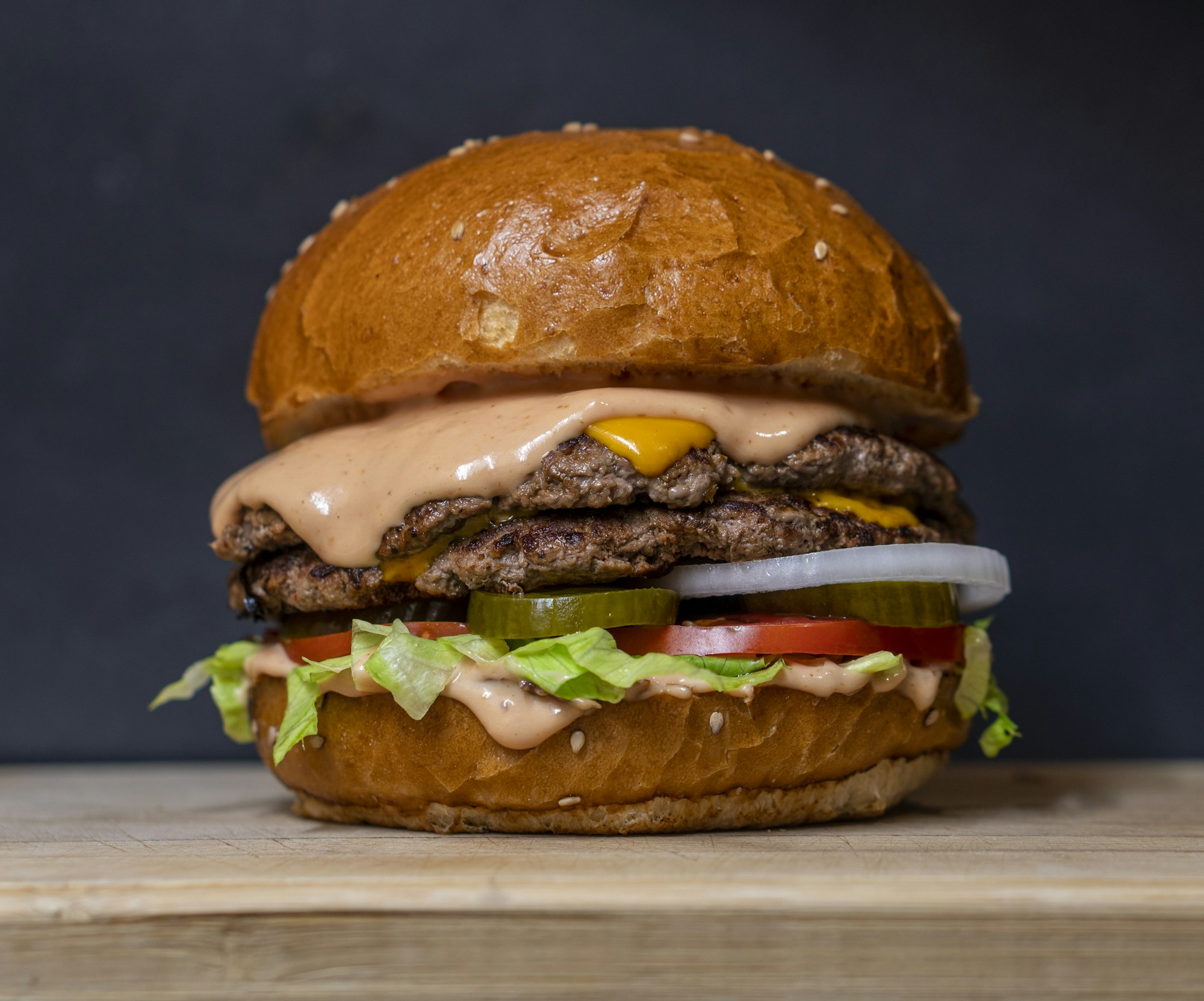 A double cheeseburger with mustard, onion and pickle on a sesame bun